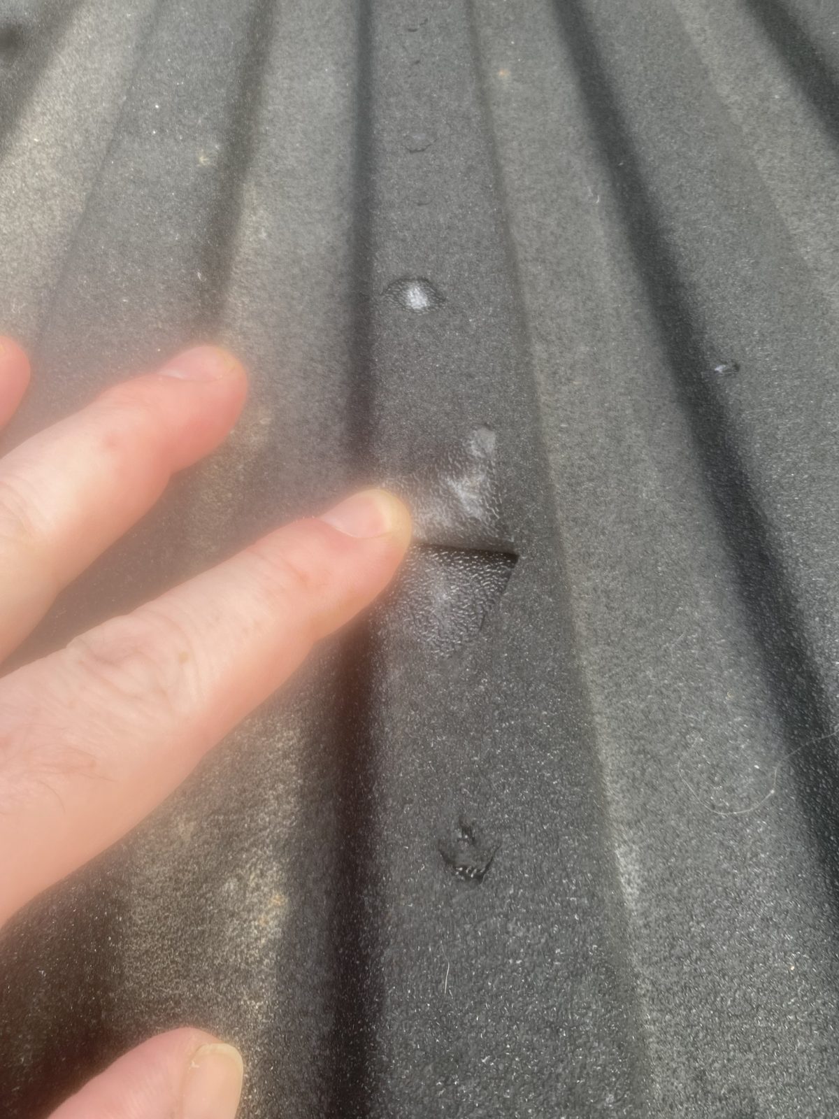 A finger lifting a loose flap of spray-in bed liner off the truck bed floor